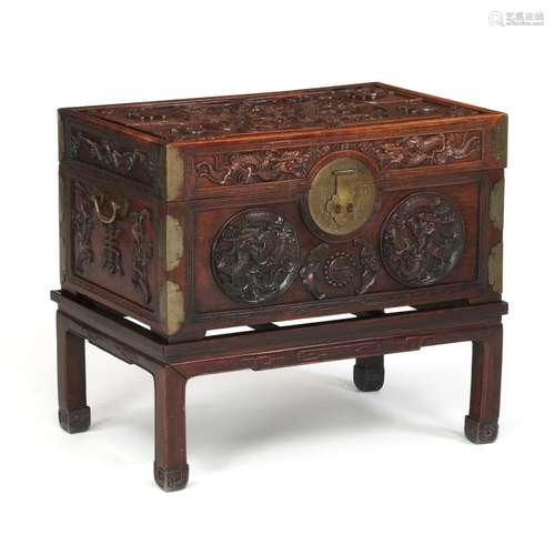 A Chinese hardwood chest on stand, the lid and sides richly carved with ornaments, brass mounting. Late Qing, late 19th century. (2)