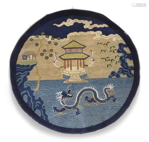 A Peking carpet, North East China. A rare circular rug depicting temple, cranes and in the foreground a five-clawed Imperial dragon. C. 1900. Diam. 145 cm.