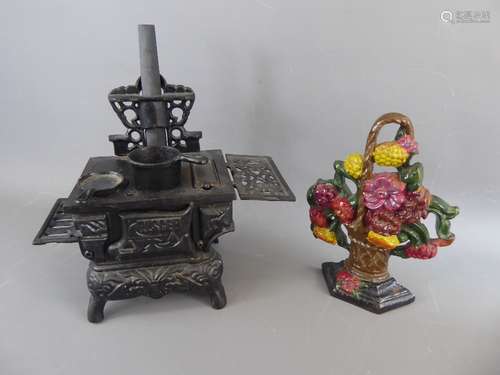 A Cast Iron Miniature Stove Door Stop, approx 30 x 14 x 31 cms, together with another door stop in the shape of a basket of red and yellow flowers approx 19 x 24 cms.