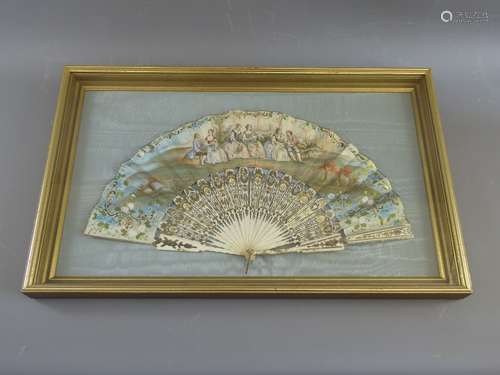 An Antique 19th Century Paper Wedding Fan, hand-painted with figures seated in a garden and gilt highlights; the fan having ivory sticks and framed on a blue silk background and glazed, approx 58 x 34 cms.