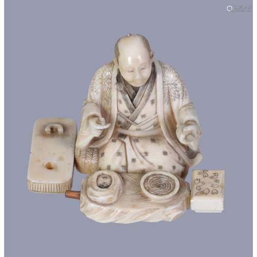 A Japanese Ivory Figure of a kneeling scholar surrounded by his inkstone and other accoutrements