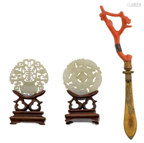 Two Chinese carved pale celadon miniature plaques on a matching wooden stand; added a red coral and gilt brass letter opener, H 9,5 - 10 cm (with stand) - L 20 cm