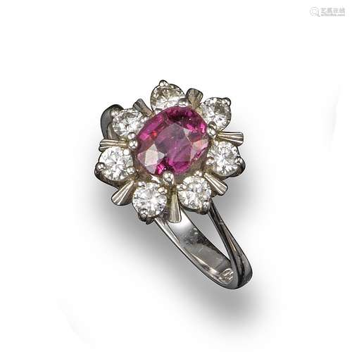 A ruby and diamond cluster ring, the oval-shaped ruby is set within a surround of circular-cut