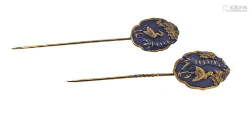 A pair of shakudo-mounted gold stick pins, each plaque depicting a standing crane with foliate, each