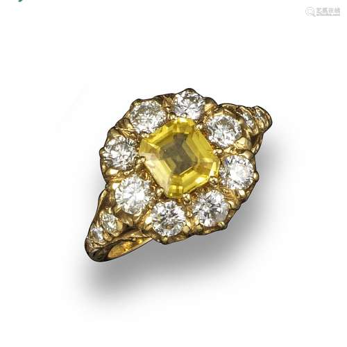 A yellow sapphire and diamond cluster ring, the emerald-cut sapphire set with round brilliant-cut