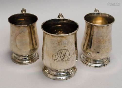 THREE GEORGE III STERLING SILVER MUGS Each with balustroid body, spreading molded foot and scrolled handle with foliate thumbpiece....
