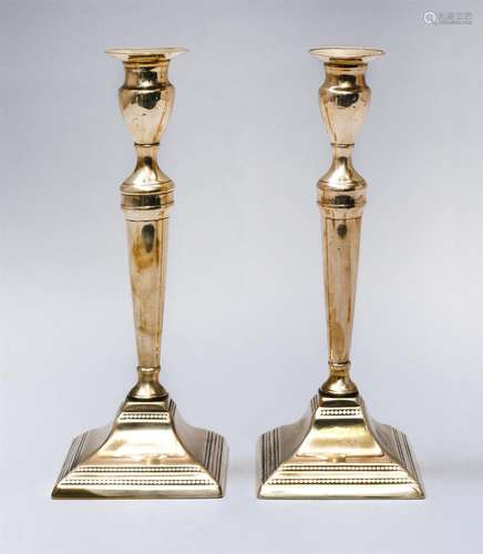 PAIR OF BELL METAL CANDLESTICKS Molded flared bobèches on tapered urns, elongated tapered shafts and square stepped molded and beade...