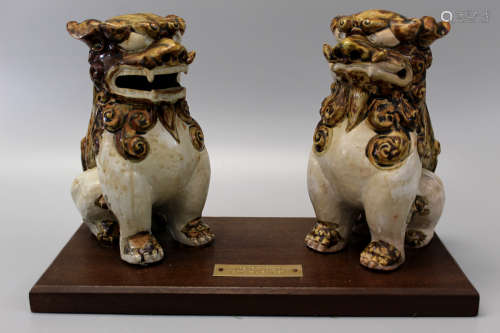 A pair of Chinese pottery Foo dogs on a wood stand.
