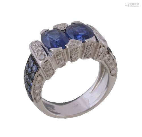 A sapphire and diamond ring, the two oval cut sapphires within a brilliant cut diamond set surround,