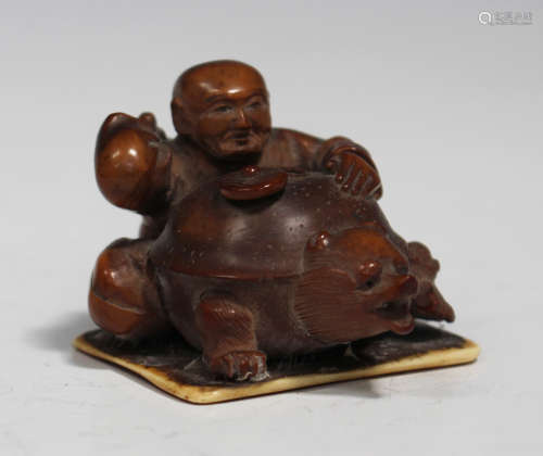 A Japanese stained ivory okimono carving, Meiji period, modelled as a seated man restraining a bear,