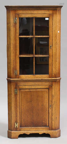 A late 20th century reproduction oak corner cabinet, the glazed door above a panelled door, on