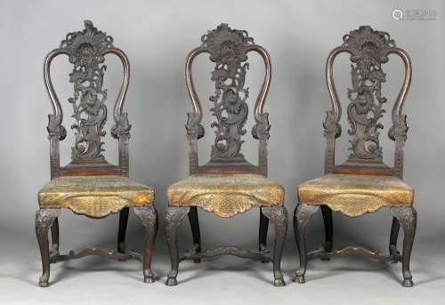A set of three mid-18th century Continental Rococo carved walnut hall chairs, each back profusely
