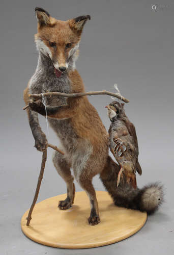 A late 20th century taxidermy specimen of a fox with a bird in its mouth, mounted on a shaped board,