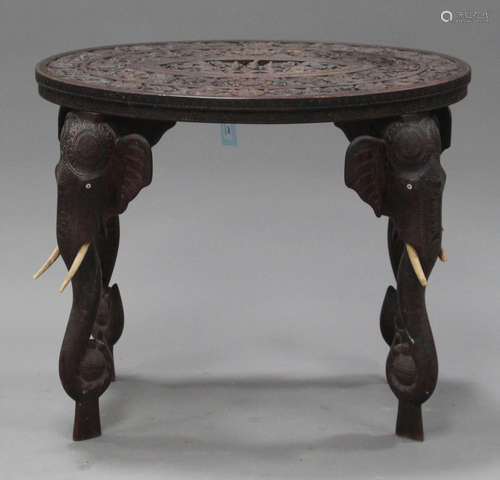 An early 20th century Indian carved hardwood oval occasional table with elephant mask legs, height