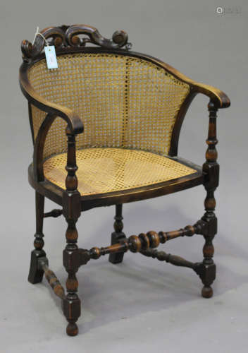 A George V walnut framed tub chair, the cane back with carved scroll surmount above a cane seat,