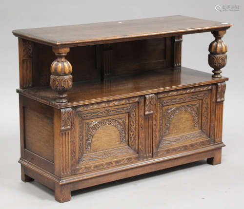 A mid-20th century oak buffet with carved decoration, fitted with a pair of panel doors, on block
