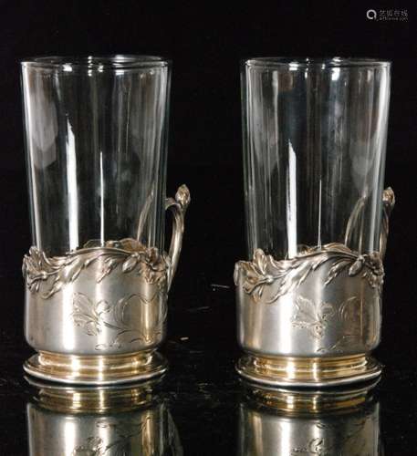 A pair of continental silver Art Nouveau tea glass holders detailed with flower and leaf borders terminating in stylised scroll handles