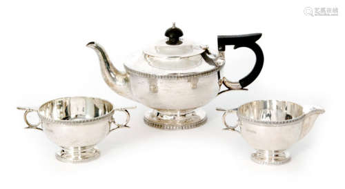 A hallmarked silver three piece pedestal tea set of plain form with stiff leaf borders