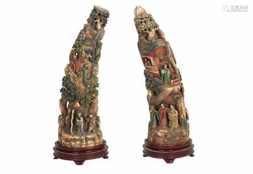 A pair of ivory tusks on wooden base, with polychrome carved decor of figures in a landscape with