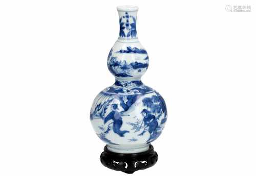 A blue and white porcelain double gourd vase on wooden base, decorated with a horseman, followed