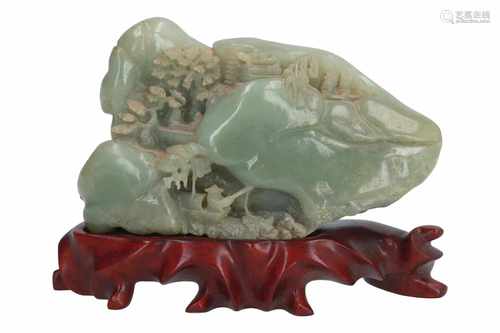 A jade carved bolder on wooden base, depicting a mountainous landscape with trees, a building and