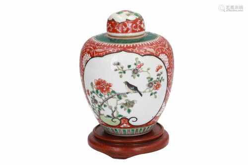 A Famille Verte porcelain lidded jar on wooden base, decorated with reserves in which birds and