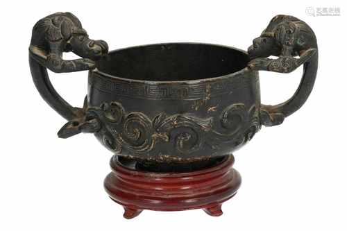 A bronze cup on wooden base, with decorations in relief and two handles in the shape of animals.