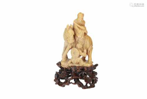 A soapstone sculpture of a figure on a horse, with a fruit seller. On carved wooden base.