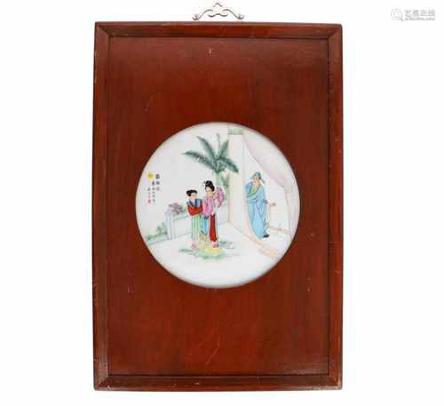 A round polychrome porcelain plaque in wooden frame, depicting two ladies and figure in a garden.