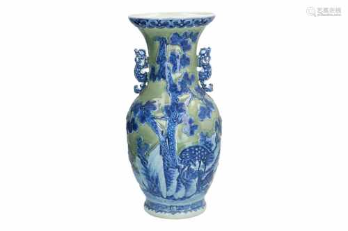 A green glazed vase with blue and white decor of a landscape and bats. The handles in the shape of