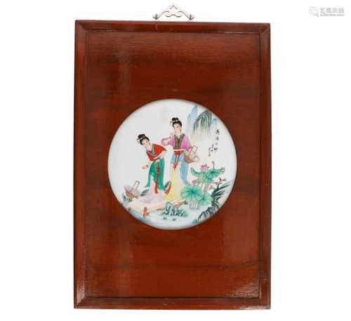 A round polychrome porcelain plaque in wooden frame, depicting two ladies near the water front.