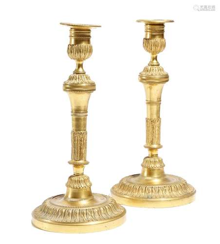 A pair of Louis XVI gilt bronze candlesticks, each with a beaded detachable drip-pan, above an urn