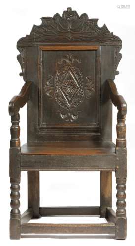 A late 17th century oak panelled back open armchair, the surmount carved with leaves, above a