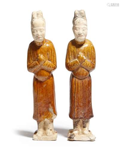 Two Chinese ochre glazed pottery figures, each wearing robes and sporting a headdress, Tang Dynasty,