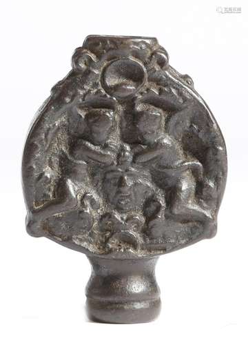 An Italian iron sword pommel, decorated on both sides with a pair of angels flanking a male mask,