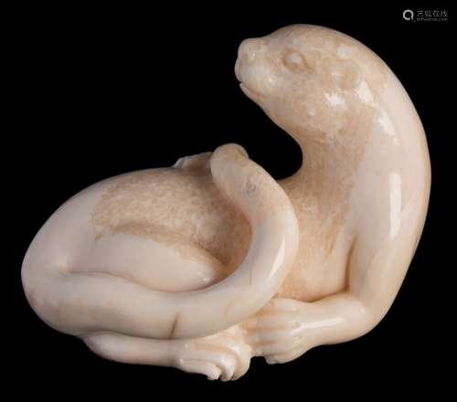 A carved fossilised marine ivory model of a sea otter: with raised head and curved tail, 8cm. long.