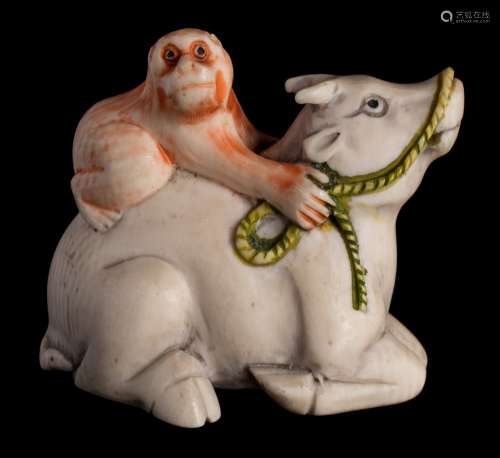 A Japanese carved and stained ivory netsuke: depicting a monkey seated on the back of an oxen,