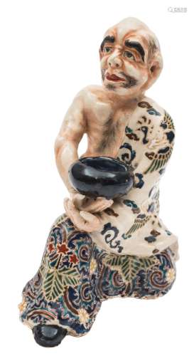 A Satsuma earthenware figure: of a kneeling bald headed monk, probably Daruma,
