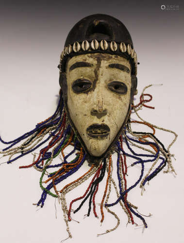 An African carved wooden mask, covered in a white pigment and applied with cowrie shells and