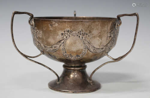 An Edwardian silver tri-handled footed bowl, decorated in relief with foliate garlands and ribbon