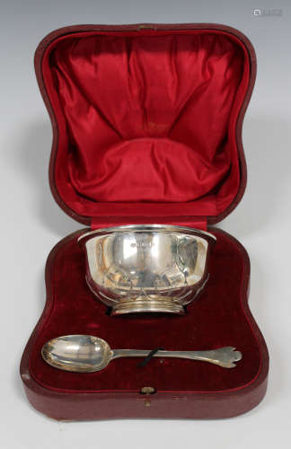 A George V silver christening bowl, decorated in relief with a band of stiff leaves, and a spoon