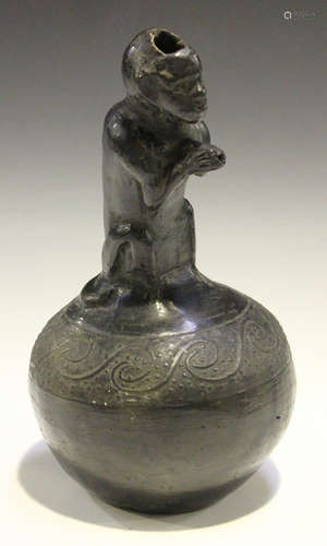 A black clay pouring vessel, probably African, the neck modelled as a seated monkey, the bulbous