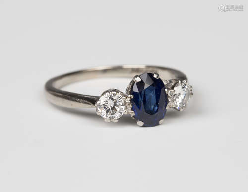 A white gold, platinum, sapphire and diamond three stone ring, claw set with the oval cut sapphire