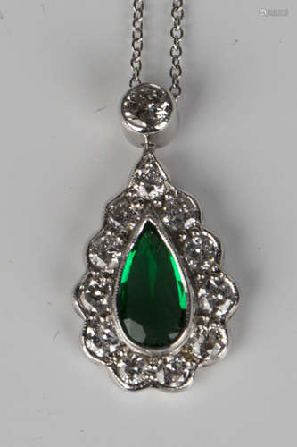 A white gold, emerald and diamond drop shaped pendant, mounted with a pear shaped emerald within a