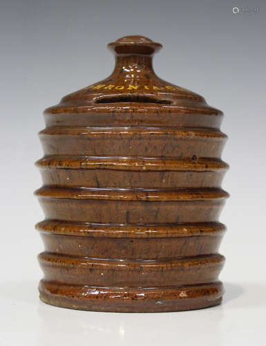 A Sussex slipware pottery money box, dated 1887, in the form of a cylindrical beehive with knop