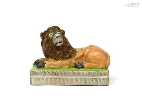 A pearlware figure of a lion early 19th century, recumbent on a rectangular base, its head turned to