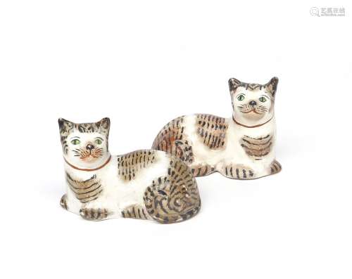 A pair of Staffordshire figures of cats 19th century, recumbent with heads turned and tails