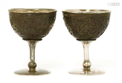 A pair of Chinese stem cups, c.1900, each bowl of carved coconut with buildings, bamboo and pine ...