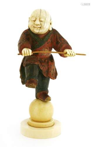 A Japanese figure, 19th century, of a boy standing with his left foot on an ivory ball, a stick in ...