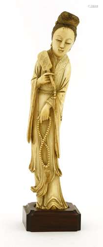 A Chinese ivory figure, late 19th century, of a lady standing with a mirror in her right hand and a ...